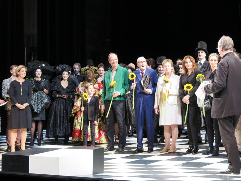 Schauspieler und Schauspielerinnen, der Regisseur und die Kostümbildnerin erhalten auf der Bühne des Opernhauses den Wanderpreis und gelbe Sonnenblumen.