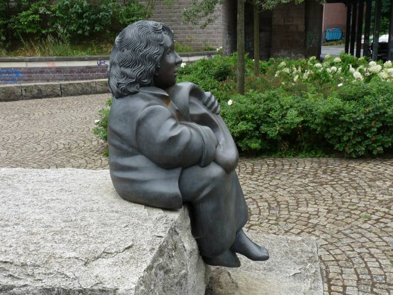 Skulptur eines sitzenden Mädchens, das ein übergroßes Ohr in den Händen hält