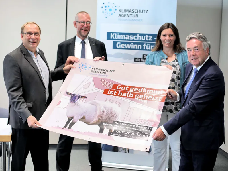 Eine Frau und drei M&auml;nner halten ein Plakat.