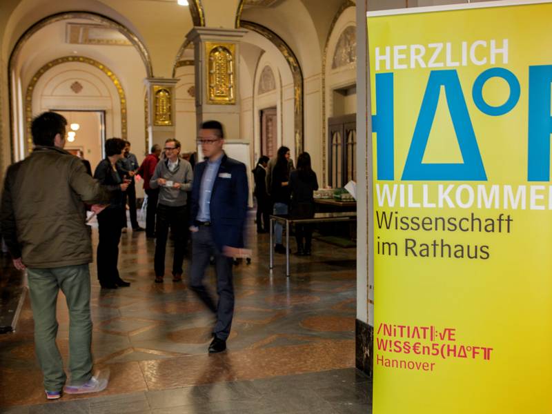 People in a hall with a stand-up display advertising the Hannover Science Initiative.