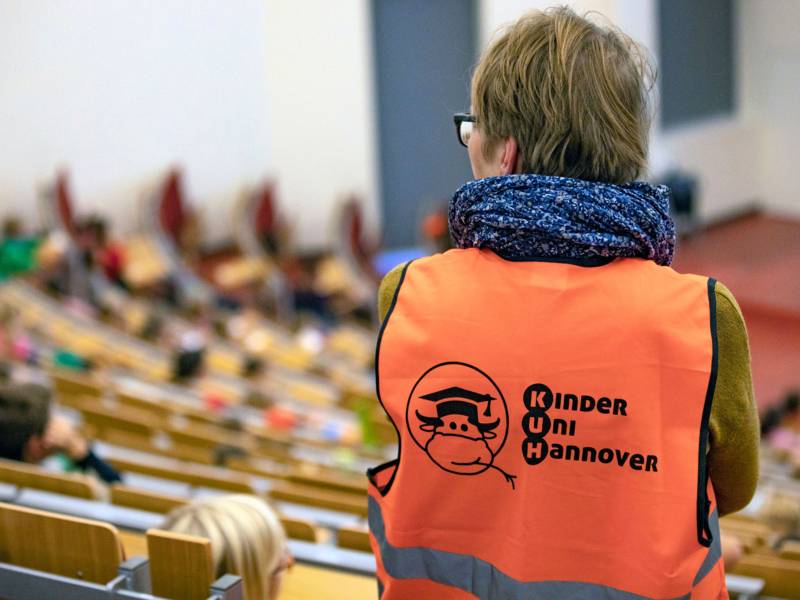 Mensch mit roter Warnweste mit der Aufschrift Kinder Uni Hannover von hinten aufgenommen