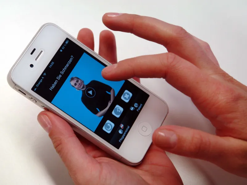 Jemand bedient ein Smartphone, auf dessen Display eine Person mit vor dem Bauch verschr&auml;nkten Armen zu sehen ist, dazu der Text: Haben Sie Schmerzen?