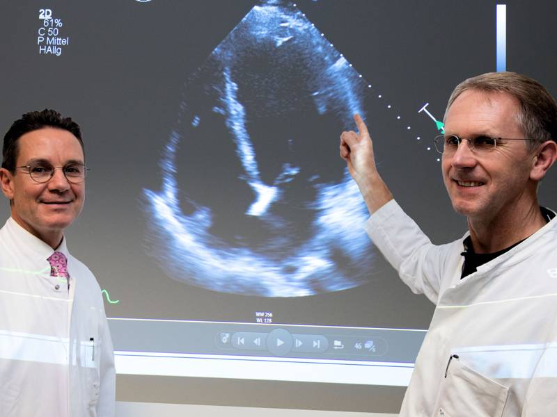 Zwei Männer in weißen Kitteln vor einem Bildschirm mit Ultraschallaufnahme.