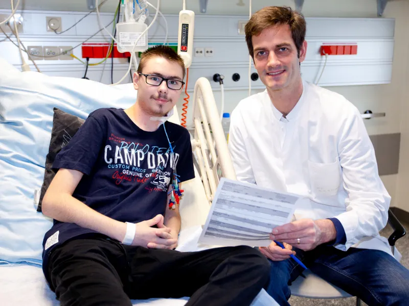 Zwei M&auml;nner sitzen auf einem Krankenhausbett.