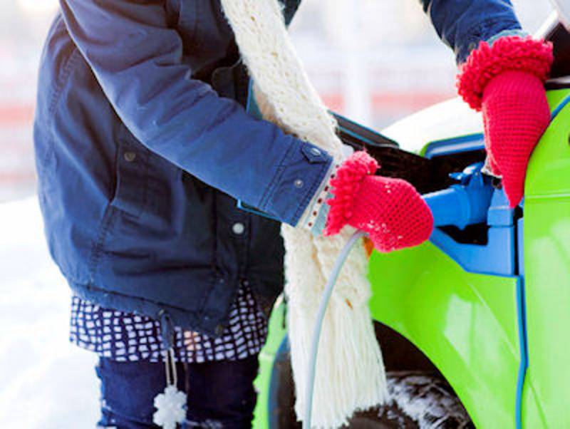 Mensch in Winterkleidung beim Laden eines E-Autos