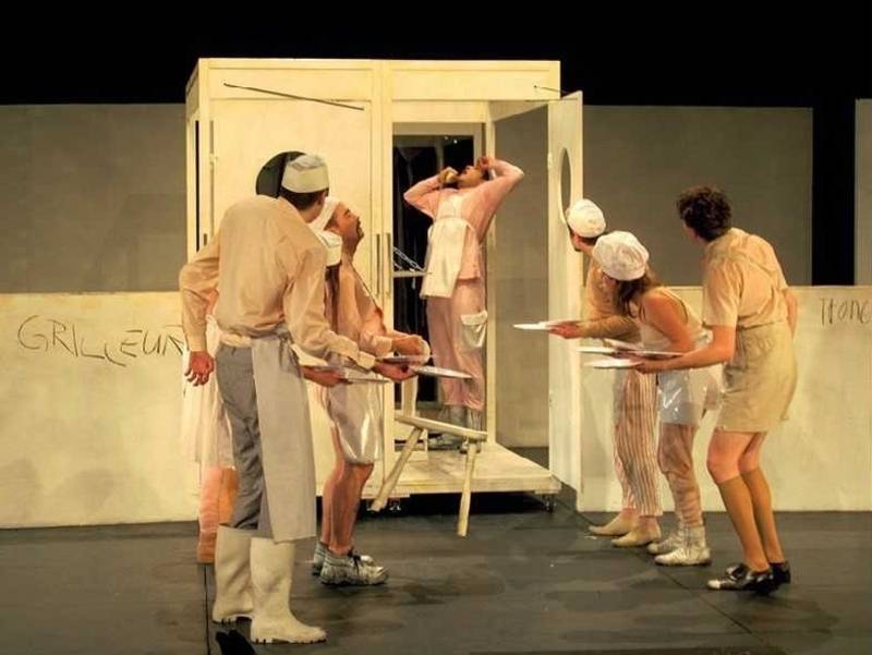 Bühne mit einem Mann in einem großen Kasten und weiteren Personen 