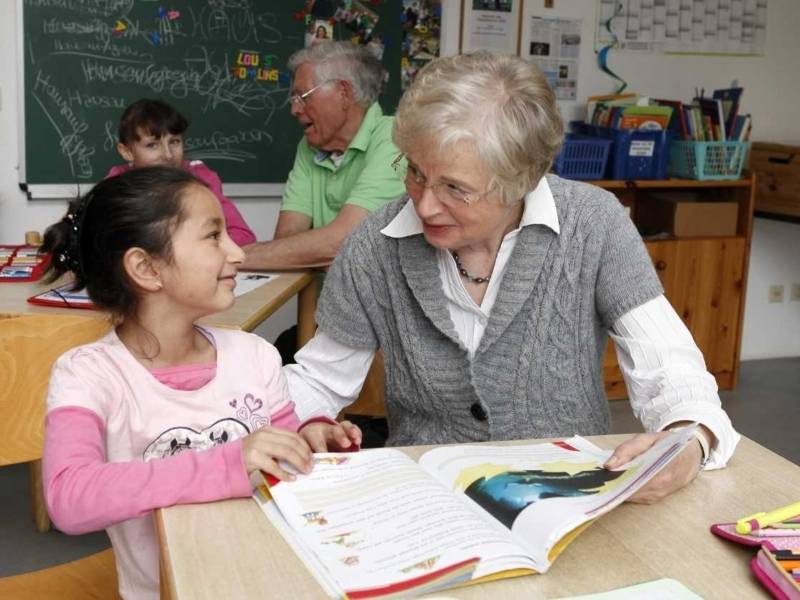 Eine ältere Frau und ein kleines Mädchen an einem Tisch mit einem Schulbuch