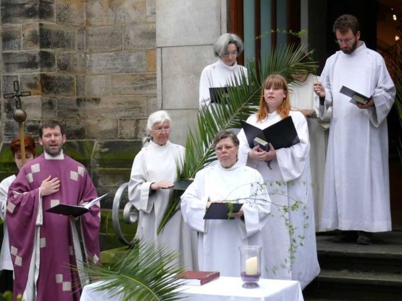 Sechs Frauen und zwei Männer in langen Gewändern vor einer Kirche