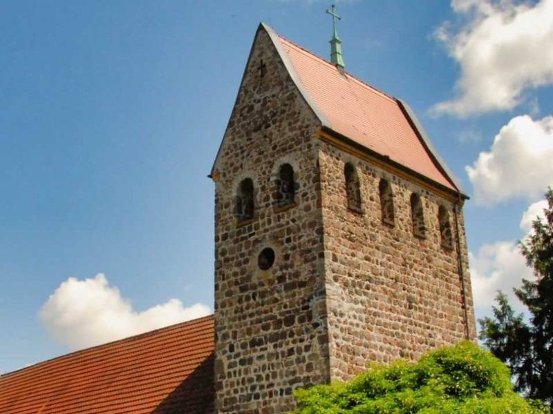 Kirchturm aus Naturstein mit Kreuz auf dem Dach