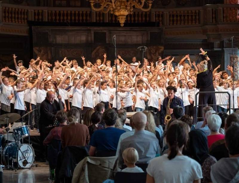 Bühne mit vielen Kindern, davor Musiker und Zuschauer