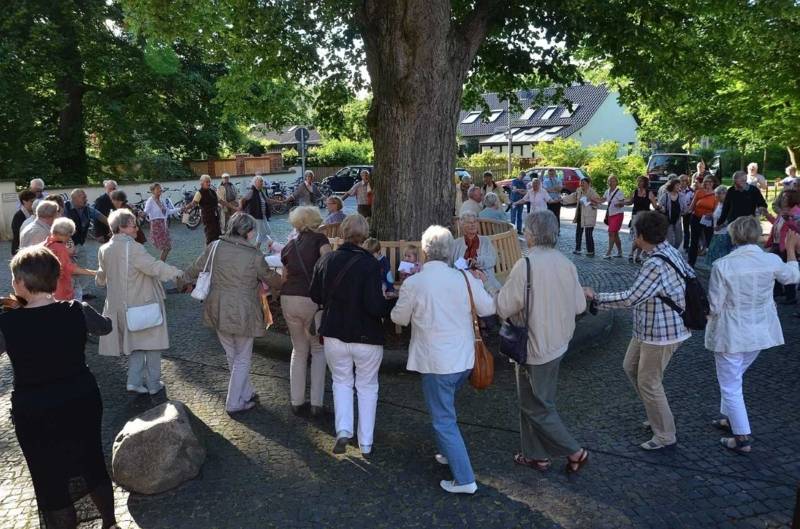 Zahlreiche Menschen bilden eine Kette um einen Baum mit Rundbank 