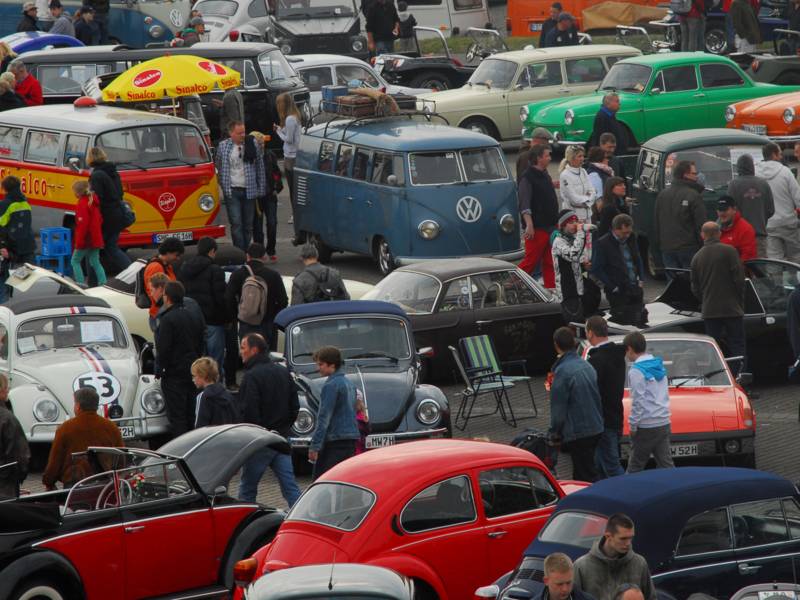 Menschen besichtigen auf einem Parkplatz viele alte VW-Käfer und andere Fahrzeugen