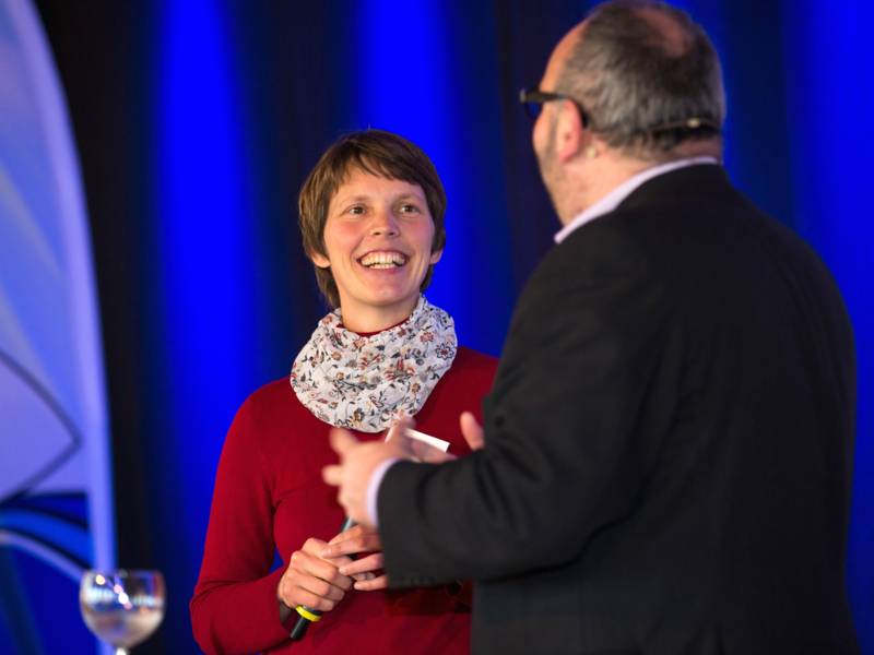 Ein Mann und eine Frau stehen auf einer Bühne und sprechen vor Publikum.