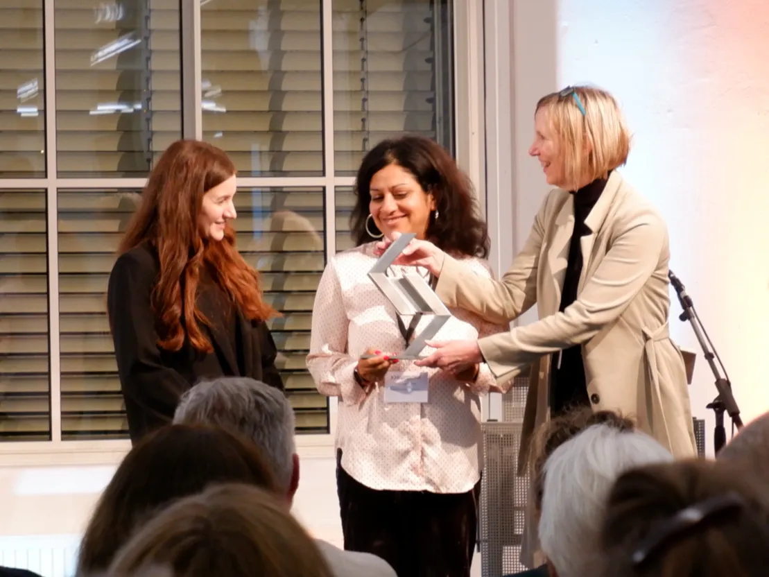 Drei Frauen stehen in einem Halbkreis. Zwei von ihnen halten eine Troph&auml;e in der Hand. Alle drei l&auml;cheln.