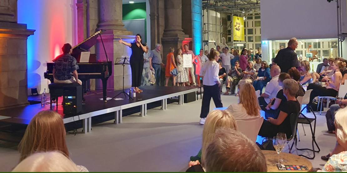 Eine Sängerin und ein Pianist stehen vor Publikum auf einer Bühne im Museum August Kestner