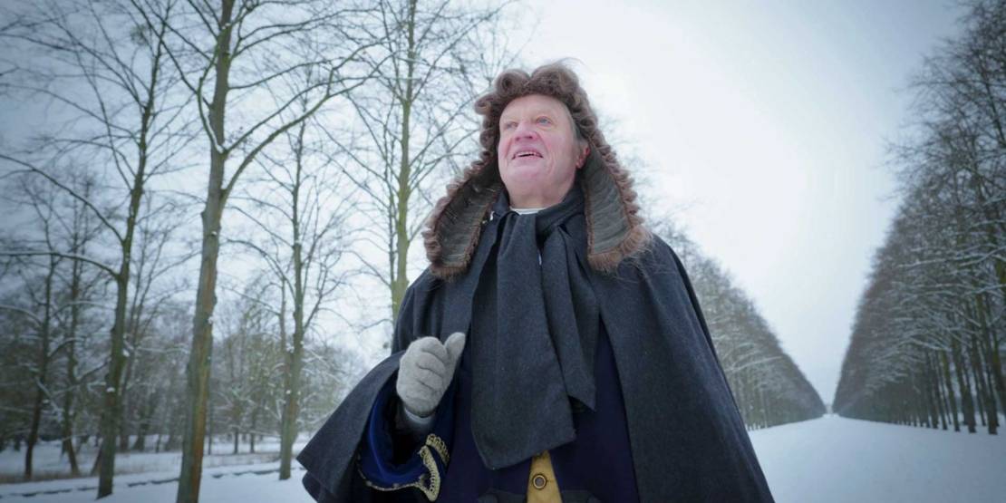 Mann mit historischer Perücke in verschneiter Allee.