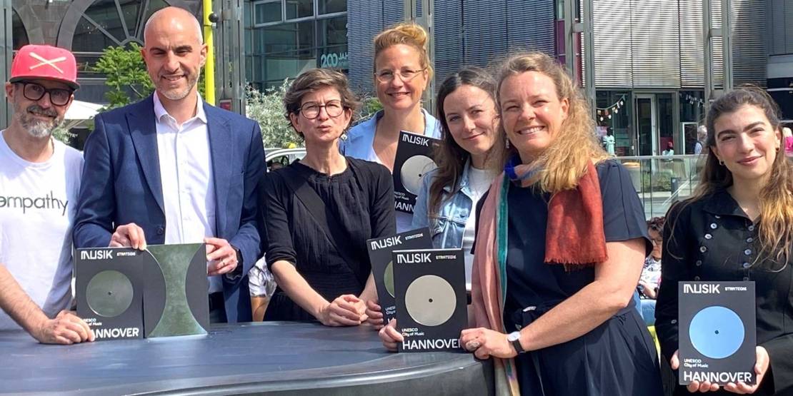 Gruppenfoto am Outdoor-Piano auf dem Opernplatz. Von links nach rechts: Rapper Spax, Oberbürgermeister Belit Onay, Friederike Ankele (Leiterin des städtischen Kulturbüros), Inga Samii (Fachbereichsleitung Kultur), Sina Hensel (Geschäftsführerin Musikland Niedersachsen), Bildungs- und Kulturdezernentin Eva Bender sowie die Sängerin und Songwriterin Amapola.