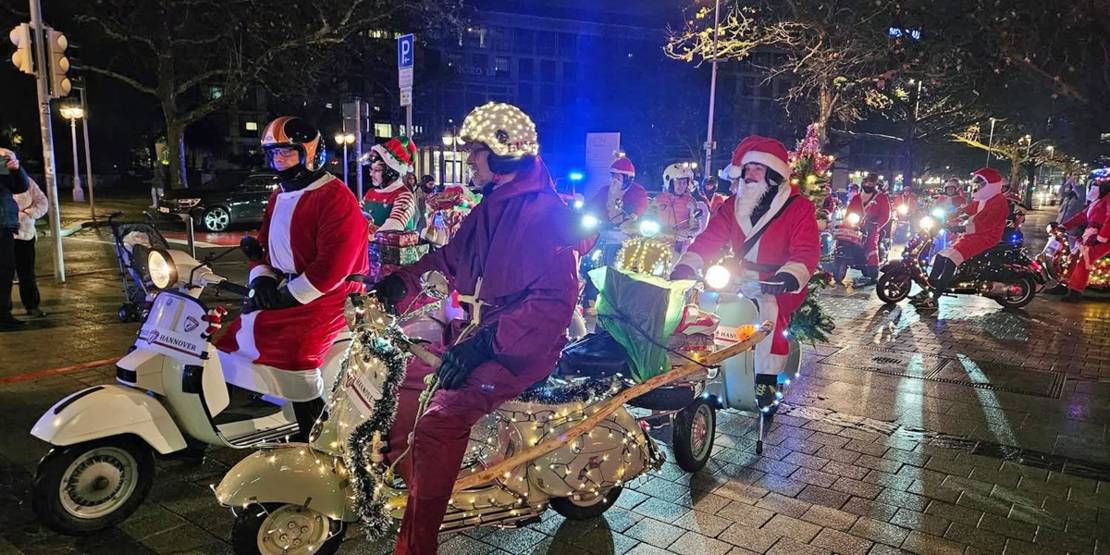 Weihnachtlich geschmücket Motorroller und Menschen verkleidet als Weihnachtsmann oder Wichtel.