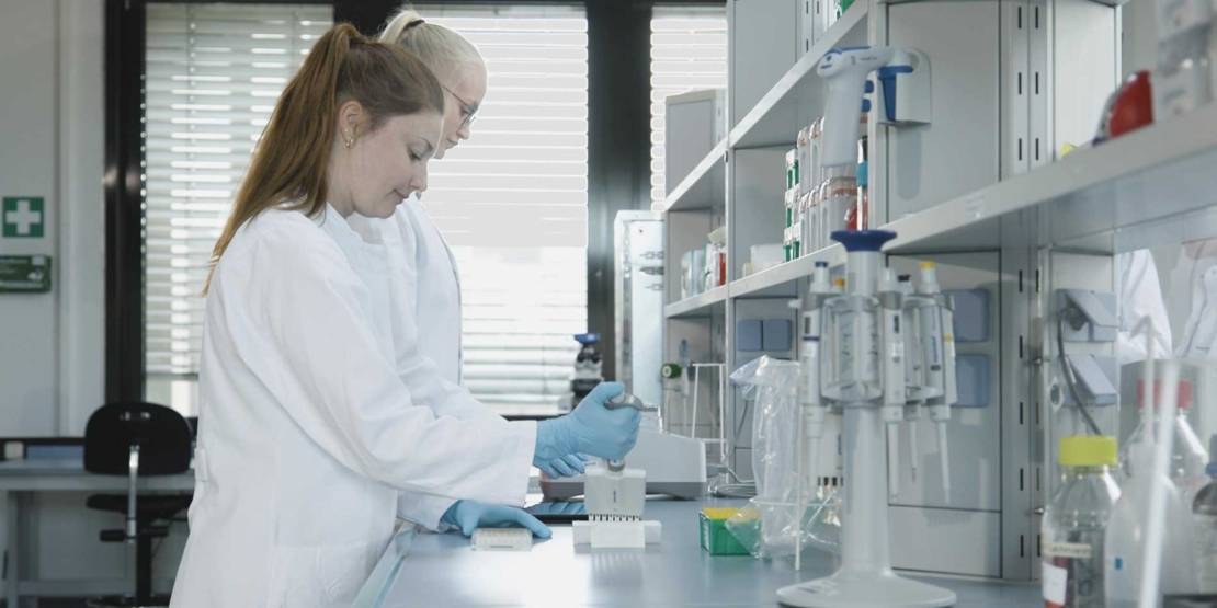 Zwei Männer und zwei Frauen in weißen Kittel gehen einen Gang entlang.