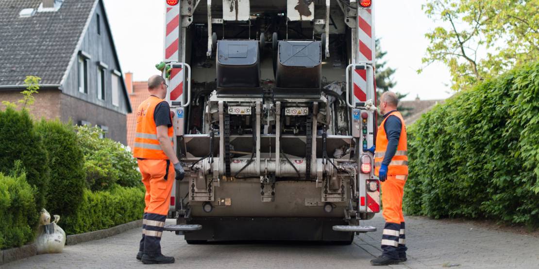 Zwei Männer in signalfarbener Arbeitskleidung an einem Müllfahrzeug.