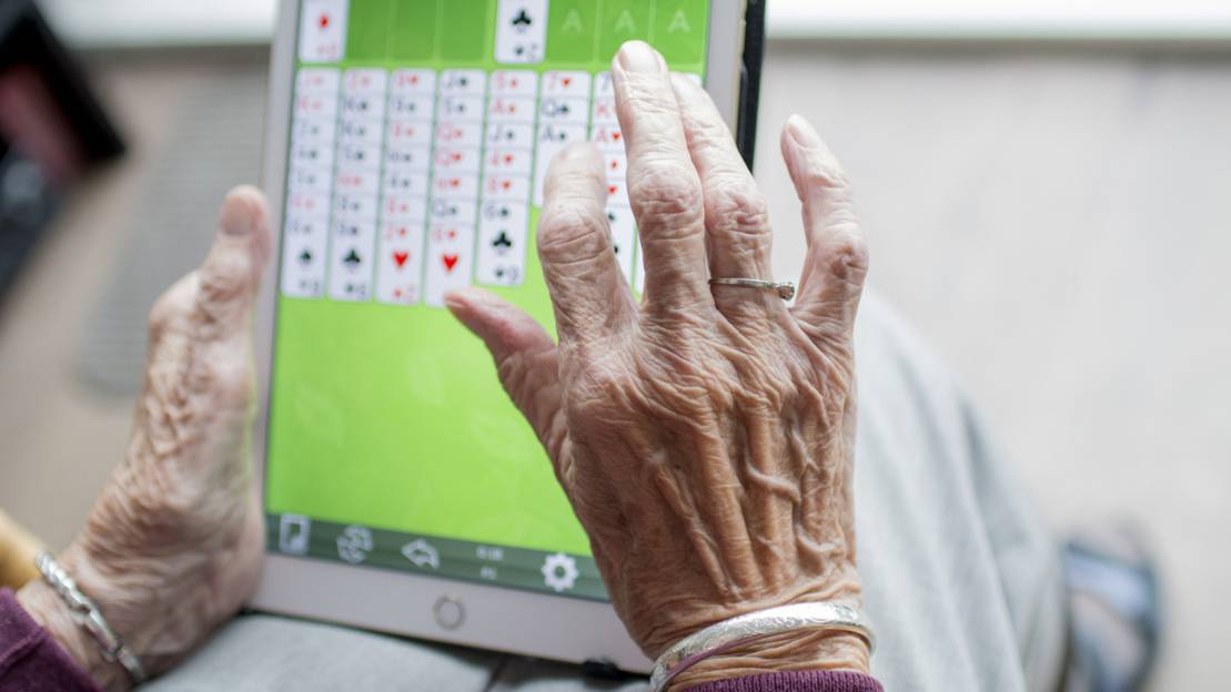 Eine Person im reiferen Alter (Falten auf den Händen) spielt auf einem Tablett das Spiel "Solitaire".