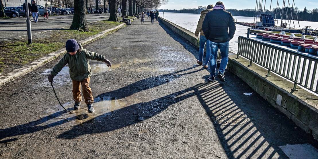 Ein Kind springt am Maschseeuferweg in eine Pfütze, im Hintergrund weitere Spaziergänger.