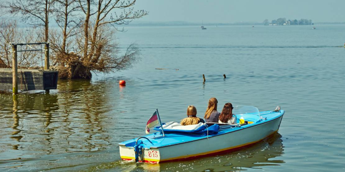 Drei Personen fahren mit einem Elektroboot vom Ufer des Steinhuder Meeres Richtung Insel Wilhelmstein.