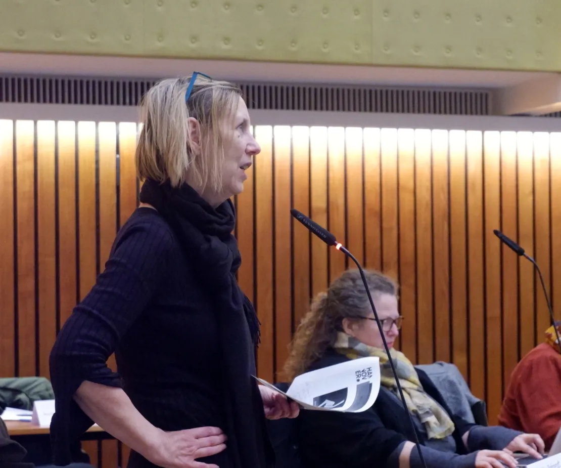 Eine Frau steht an einem Mikrofon. Sie hat blonde Haare und stemmt eine Hand in die H&uuml;fte.