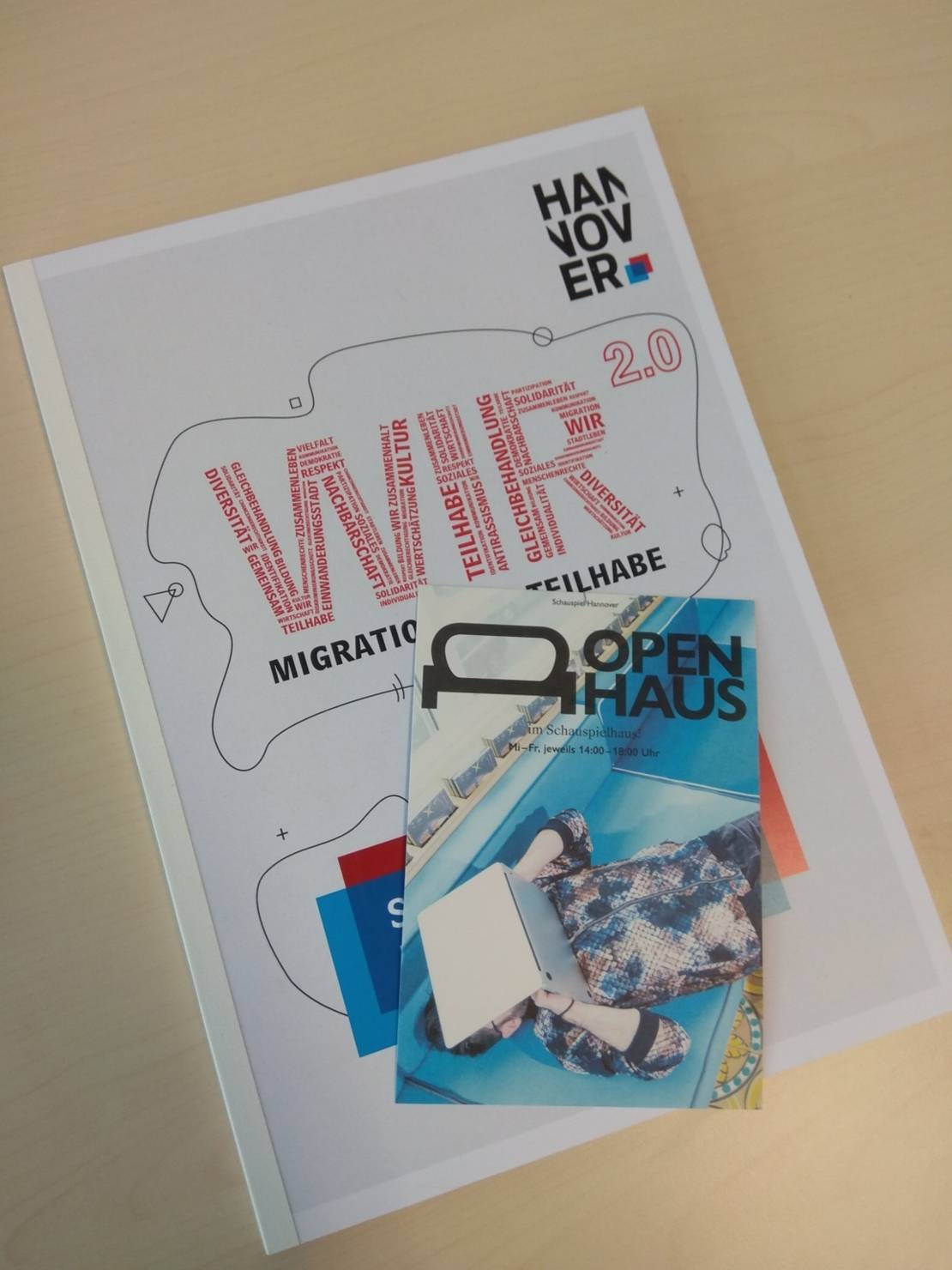 Ein in Blau gehaltener Flyer mit der Aufschrift "Open Haus" liegt auf dem WIR2.0-Maßnahmenkatalog