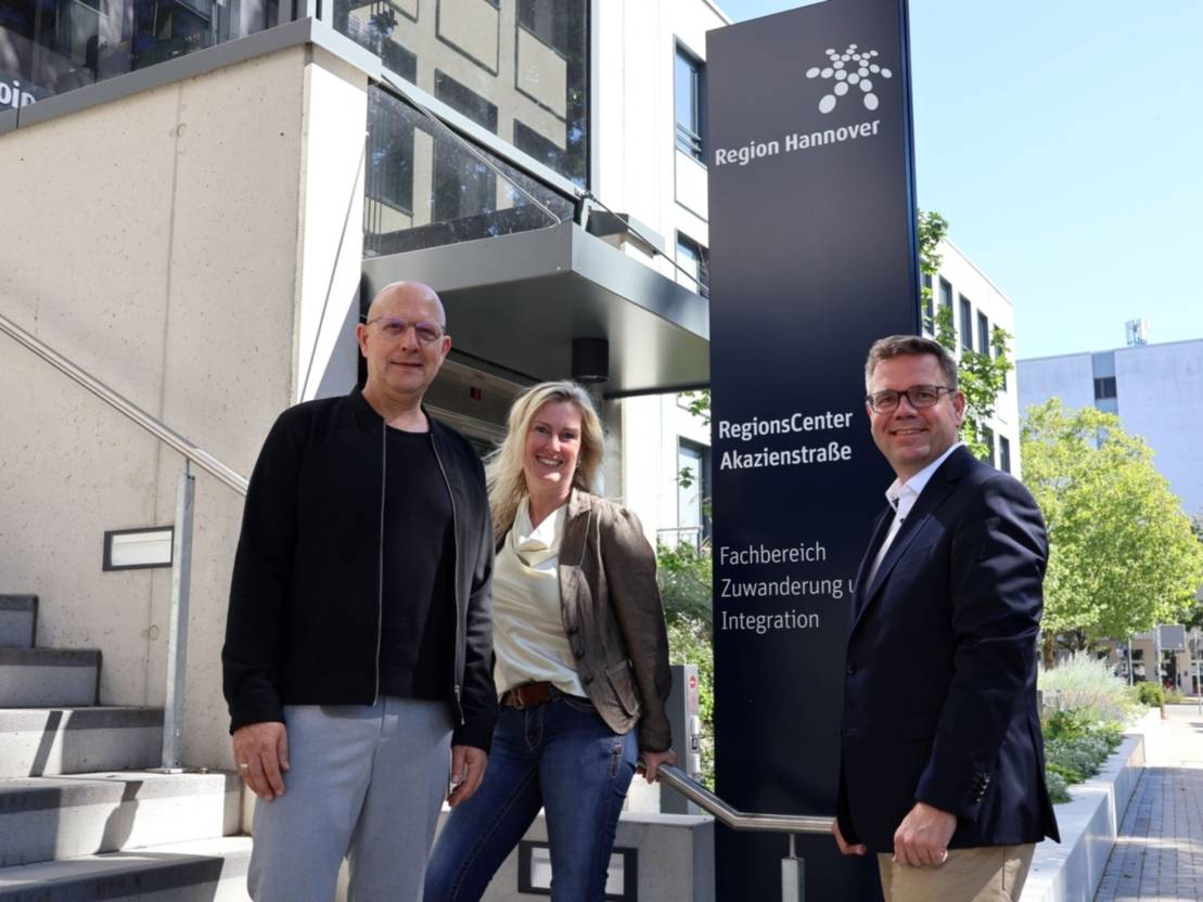 Zwei M&auml;nner und eine Frau stehen repr&auml;sentativ neben einem Schild, auf dem steht: RegionsCenter Akazienstra&szlig;e