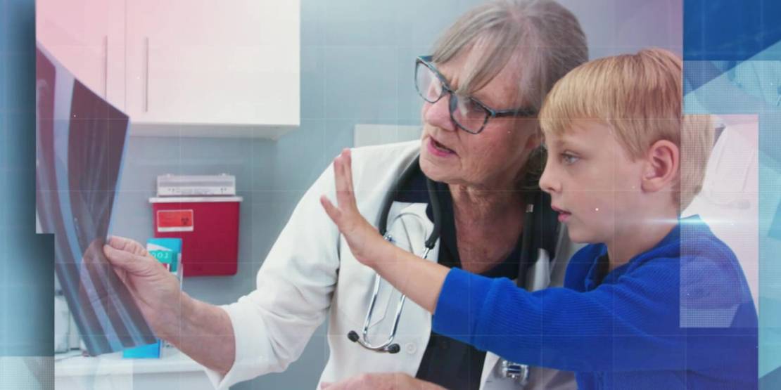 Frau in weißem Kittel zeigt einem Kind etwas auf einer Röntgenaufnahme.