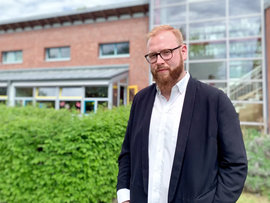 Portrait eines Mannes vor einer Hecke und einem Geb&auml;ude.