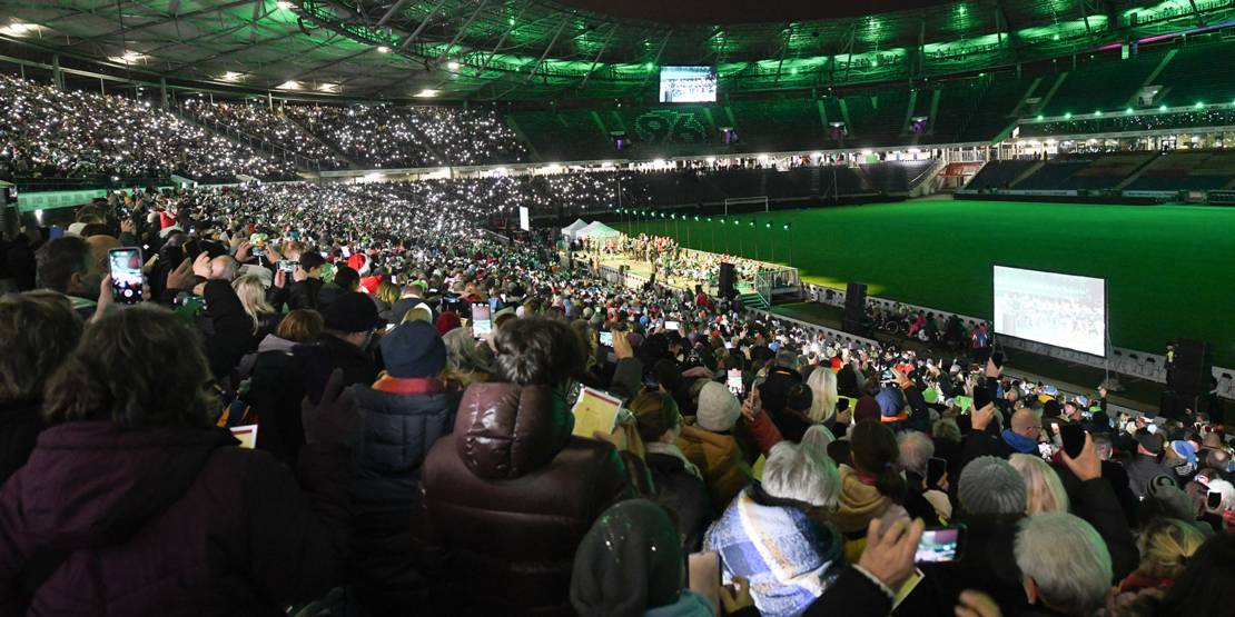Zahlreiche Menschen sitzen auf einer Stadiontribüne und halten Lichterkerzen in die Luft.