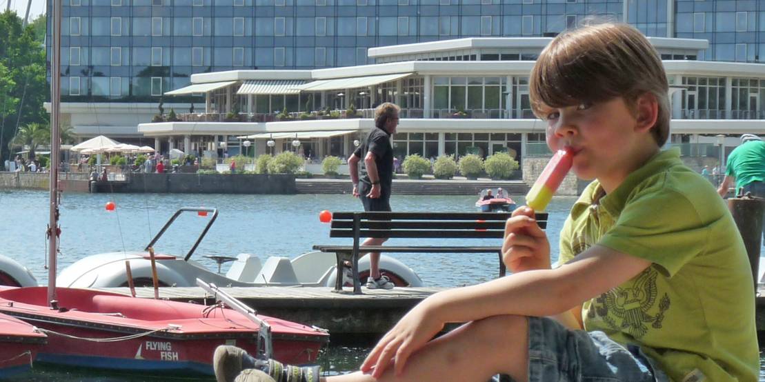 Junge sitzt auf Steinmauer am Maschseeufer und ist ein Eis