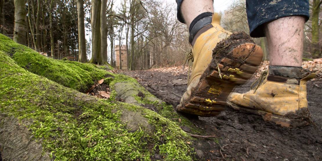 Matschiger Waldweg auf dem jemand mit dreckigen Wanderschuhen geht