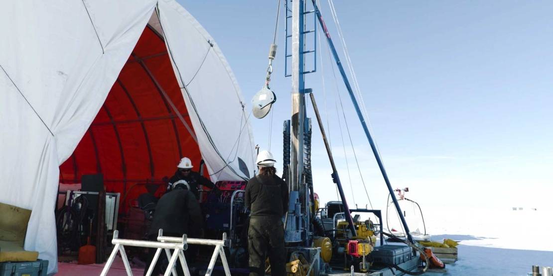Wissenschaftler mit Sedimentbohrer in Eislandschaft.