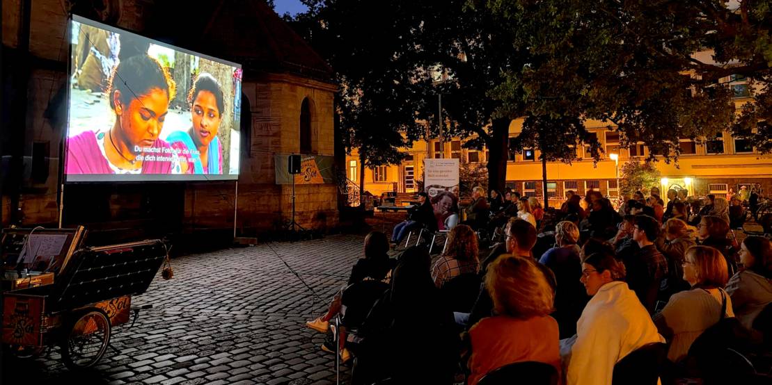 Publikum blickt bei Open-Air-Kino auf eine Leinwand.