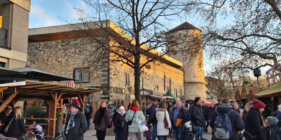 Die alte Stadtmauer von Hannover mit dem Beginenturm, davor Menschen an Ständen des mittelalterlichen Dorfs des Weihnachtsmarkts