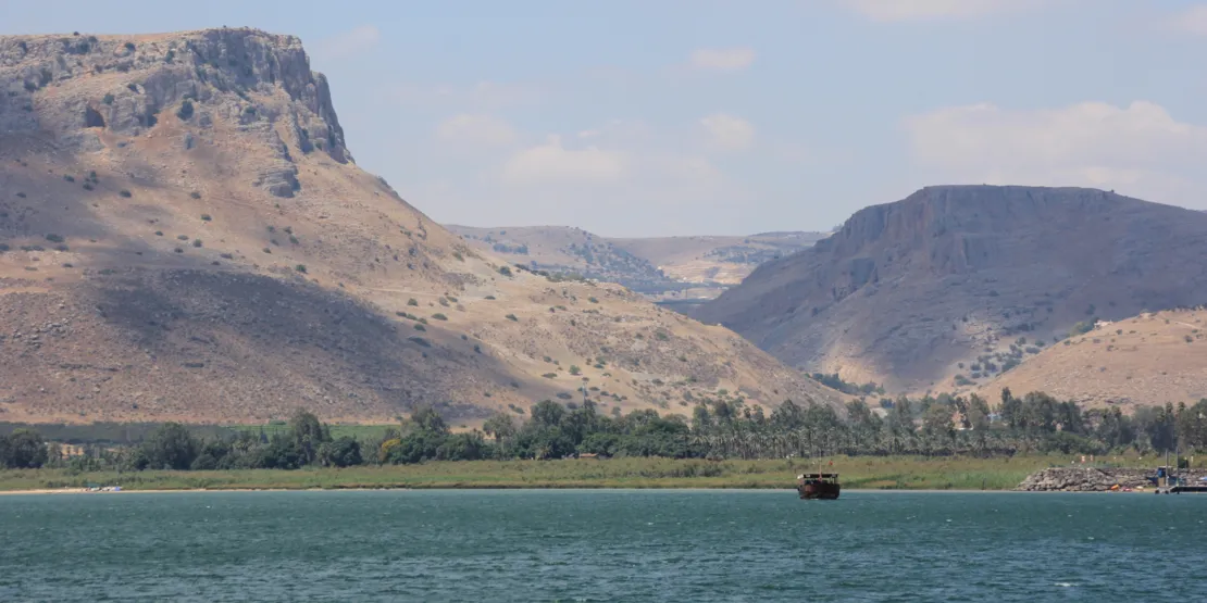 Im Vordergrund ein See mit einem Boot, im Hintergrund recht karge, aber imposante Berglandschaft