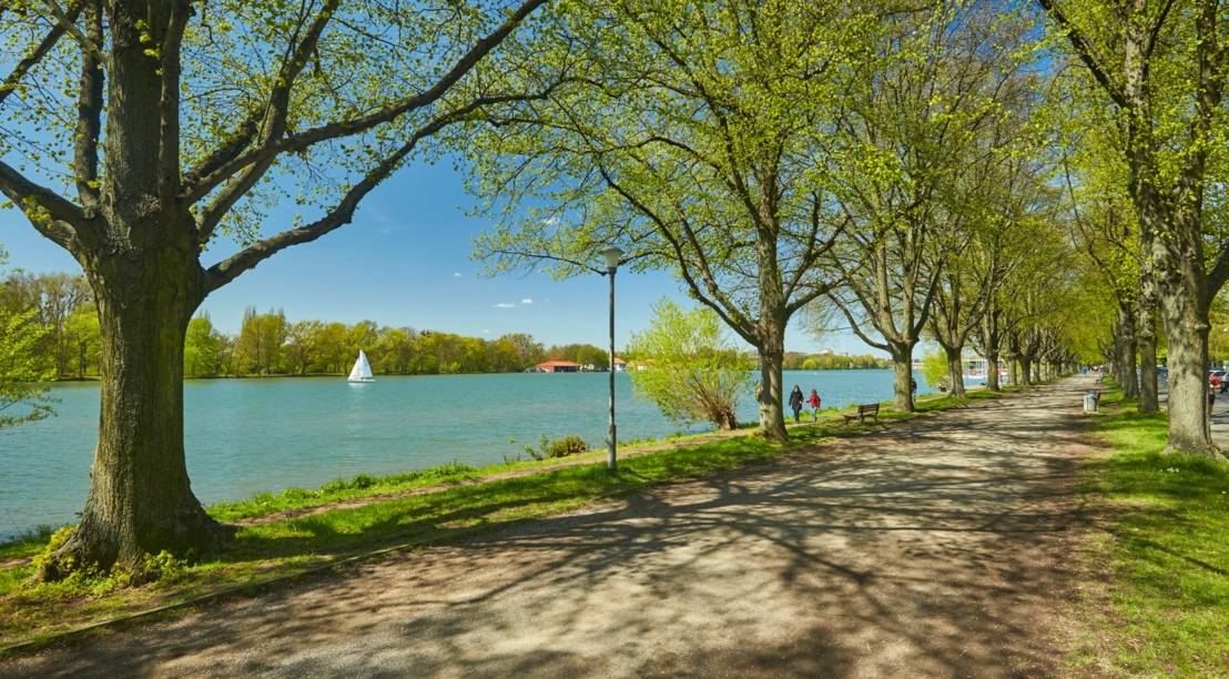 Ufer eines Sees mit grünen Bäumen und Spaziergängern im Frühling