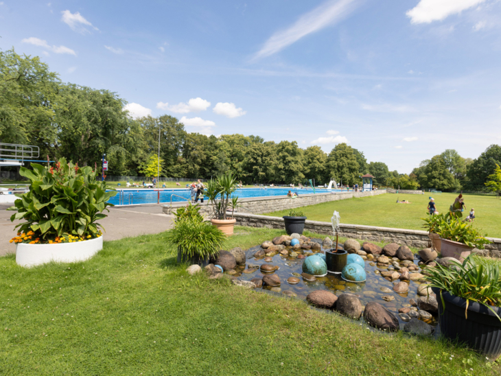 Springbrunnen, Rasenflächen, Kübelpflanzen, im Hintergrund ein Schwimmbecken