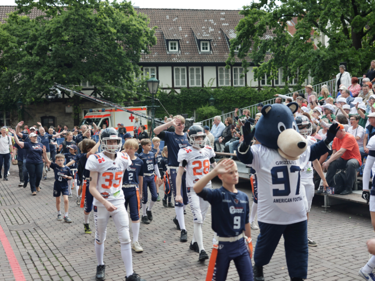 Menschen bei einem Festumzug. Im Hintergrund einer Tribüne voller Menschen.