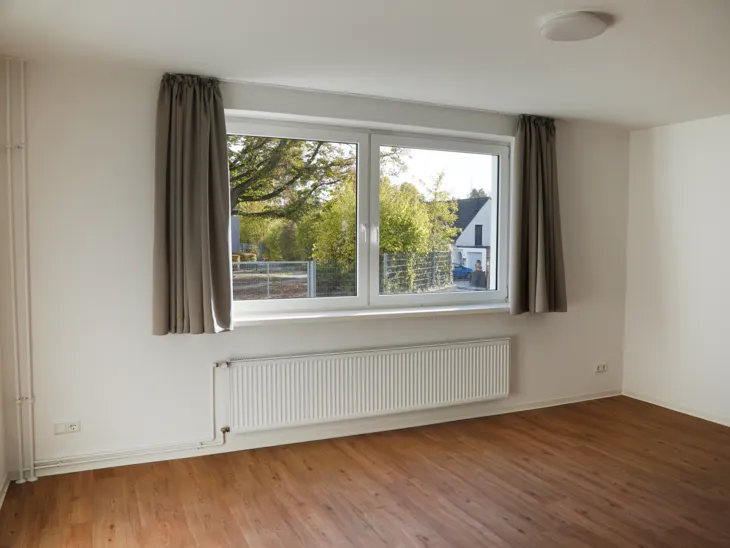 Ein heller leerer Raum mit einem Fenster und Vorhängen, Fußboden in Holzoptik.