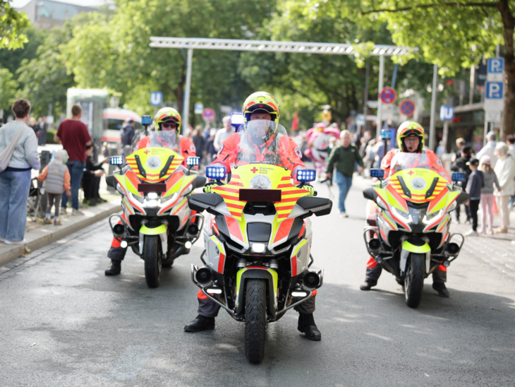 Drei Menschen auf Motorrädern in einem Festumzug.
