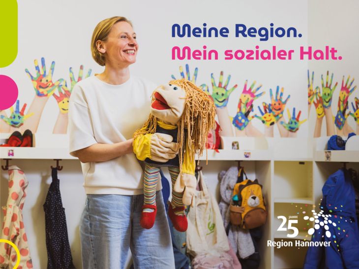 Eine Frau steht in einer KiTa vor der Garderobe mit Kinderjacken und spielt mit einer Handpuppe.