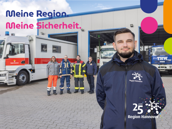 Ein Mitarbeiter des Katastrophenschutz-Teams steht vor einer Halle mit Einsatzfahrzeugen von THW und Rettungsdienst der Region Hannover.