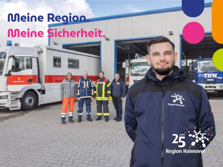 Ein Mitarbeiter des Katastrophenschutz-Teams steht vor einer Halle mit Einsatzfahrzeugen von THW und Rettungsdienst der Region Hannover.