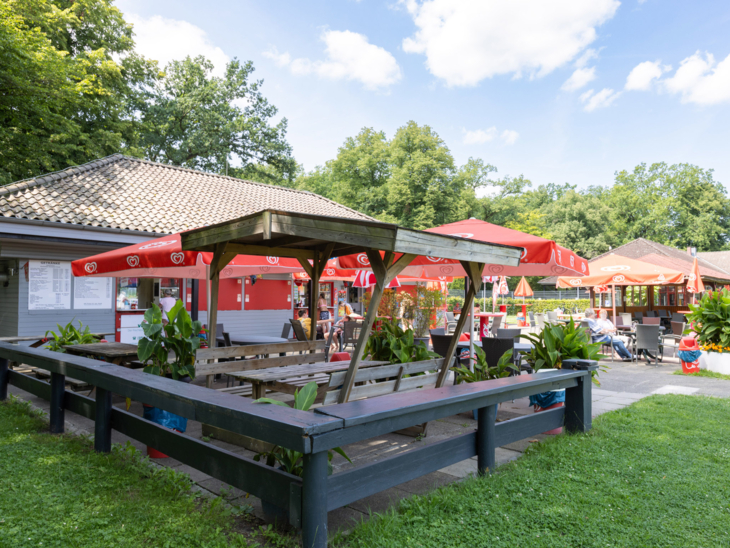 Bistro im Freibad mit Holztischen und Bänken, sowie Sonnenschirmen