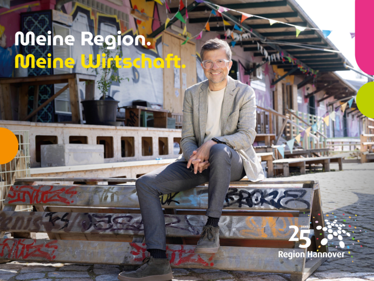 Ein Mann mit Sakko sitzt in einem ehemaligen Industriegelände mit bunten Graffitis und Girlanden.