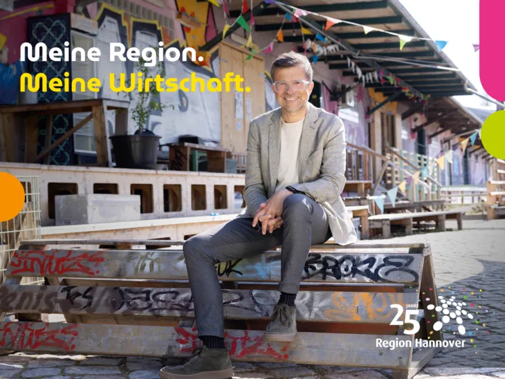 Ein Mann mit Sakko sitzt in einem ehemaligen Industriegelände mit bunten Graffitis und Girlanden.